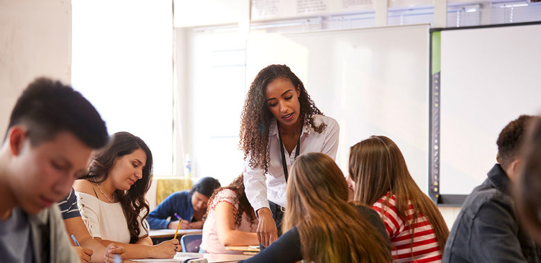 Lärare står vid ett bord där det sitter elever och lyssnar