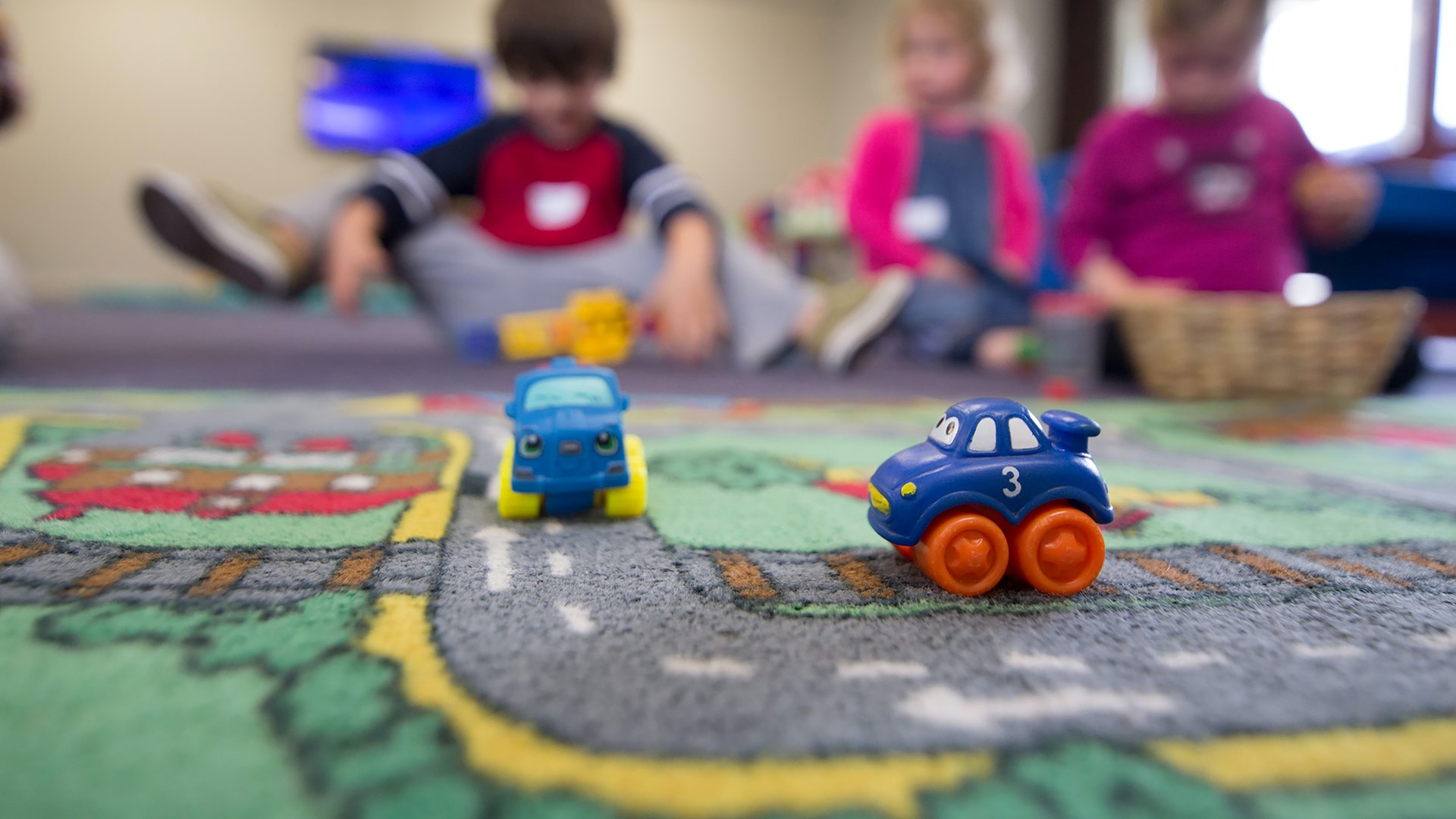 Två leksaksbilar på ett golv med lekande barn i bakgrunden